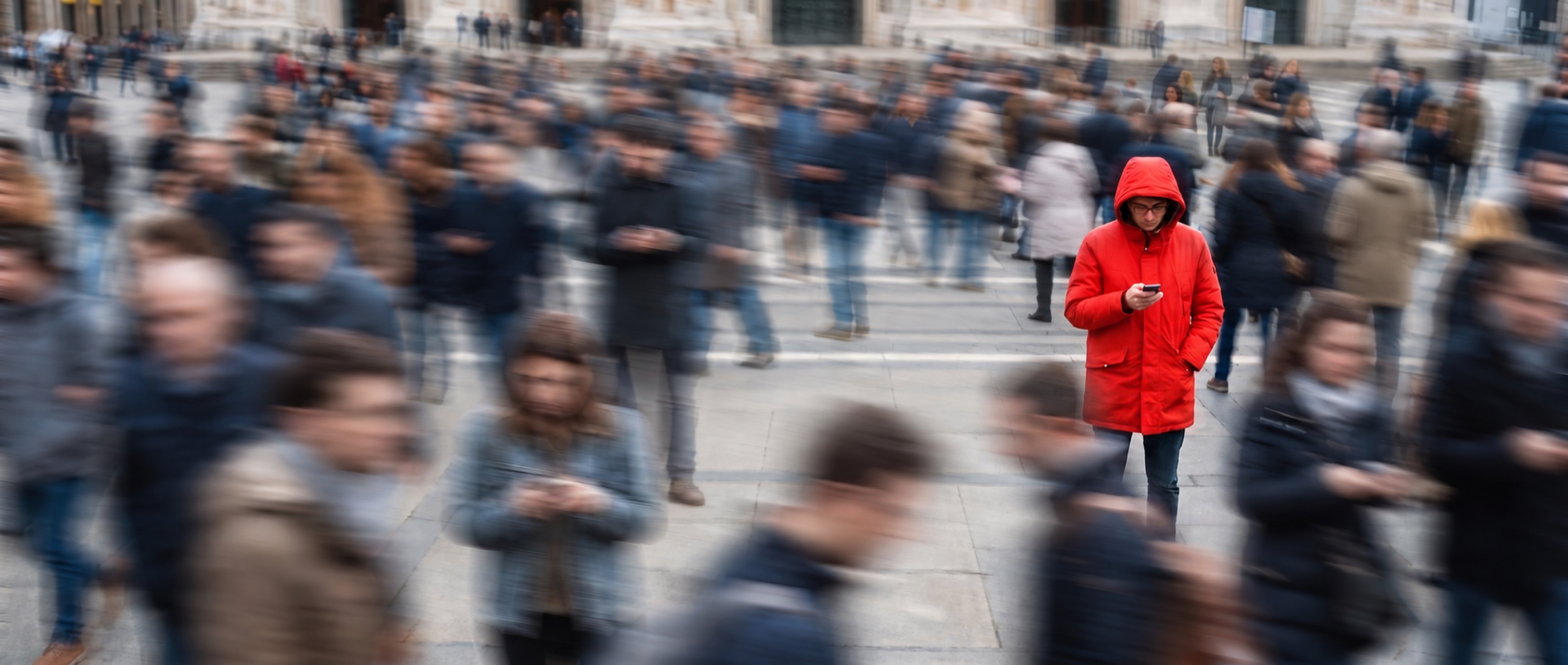 Menschenmenge auf einem Platz, in Bewegung verwischt — eine Person in roter Jacke steht still über ihrem Smartphone